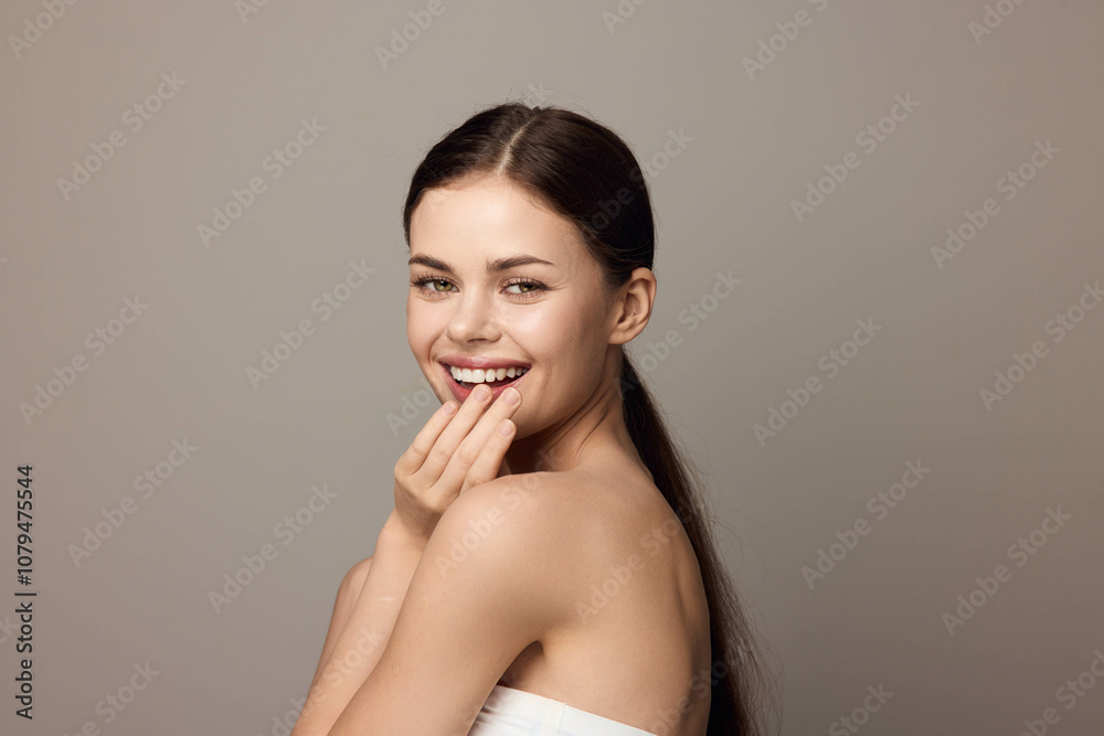 Beautiful young woman smiling while covering her mouth with her hand on a gray background Beautiful young woman smiling while covering her mouth with her hand on a gray background