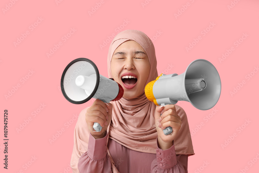 Young Asian Muslim woman shouting into megaphones on pink background. National Be Heard Day Young Asian Muslim woman shouting into megaphones on pink background. National Be Heard Day