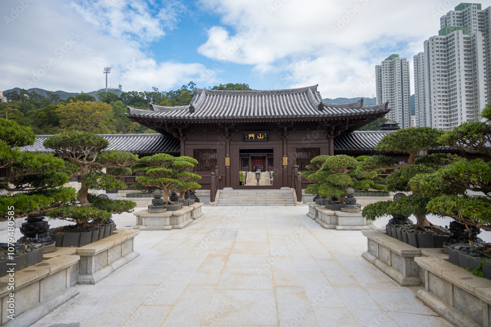 Chi Lin Nunnery entrance with a brown wooden structure and a tiled roof, flanked by rows of bonsai trees in stone planters. The path leading to the temple is paved with gray stone tiles. Chi Lin Nunnery entrance with a brown wooden structure and a tiled roof, flanked by rows of bonsai trees in stone planters. The path leading to the temple is paved with gray stone tiles.
