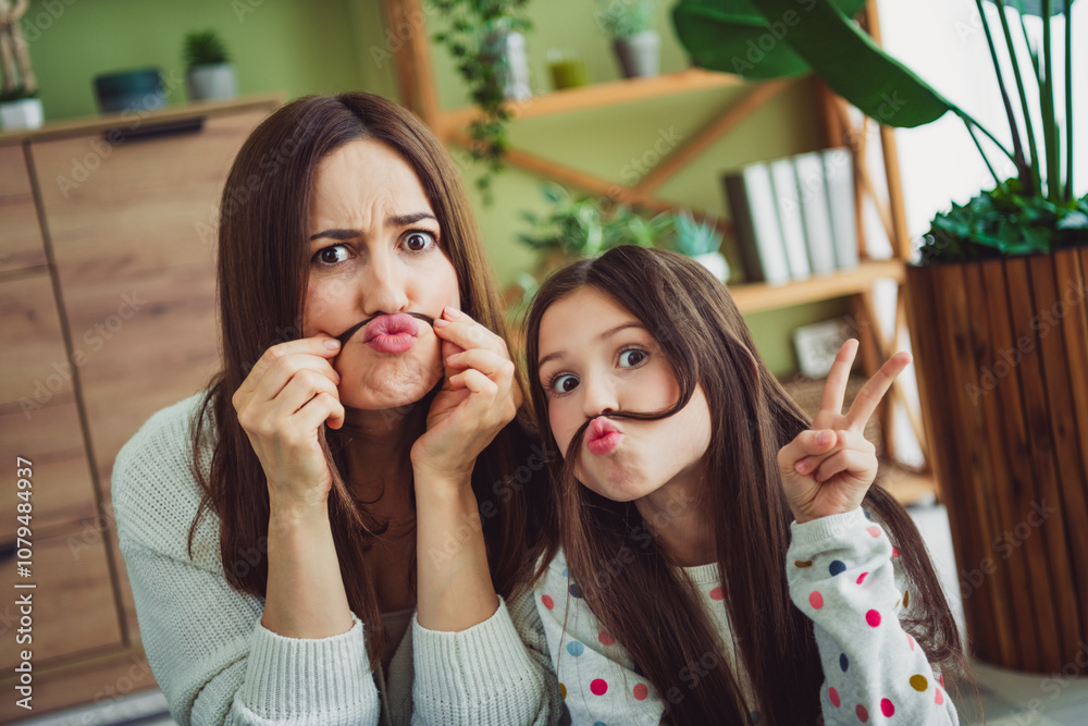 Playful young mother and daughter making funny faces in cozy living room Playful young mother and daughter making funny faces in cozy living room