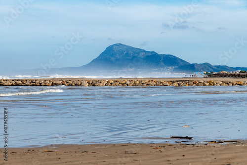 Wide Sandy Beach with Calm Water, Mountain and Coastal Buildings photo