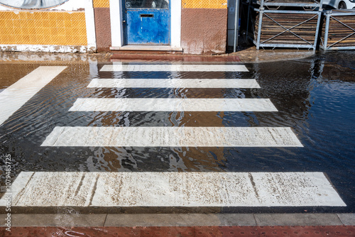 Flooded crosswalk with reflections and a worn blue door in the background photo