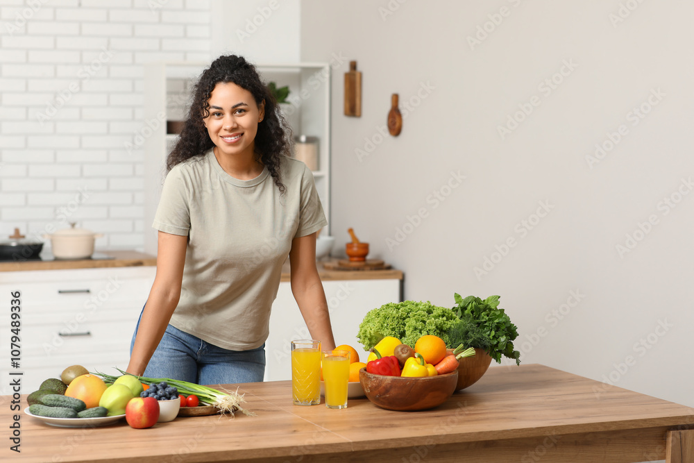 Young happy African-American woman with glasses of juice, different vegetables and fruits in kitchen. Independence from Meat Day Young happy African-American woman with glasses of juice, different vegetables and fruits in kitchen. Independence from Meat Day