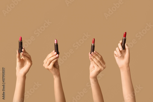 Female hands with many lipsticks on brown background