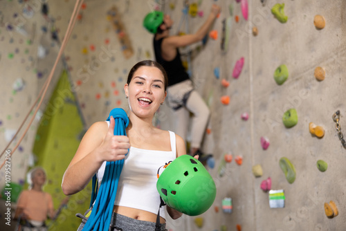 young woman after successful rock climbing session in gym smiling satisfactorily and showing thumbs up photo