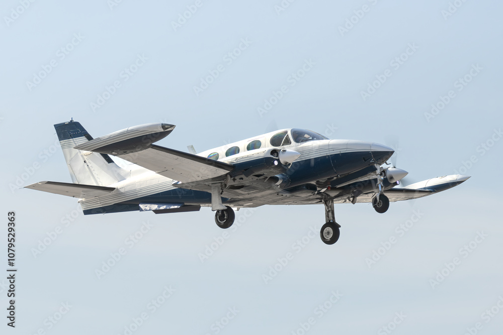 Fototapeta premium Twin Engine Aircraft during climb out. Blue and white multi with retractable gear and two propellers departs the airfield for bluer skies. Isolated airplane flying overhead