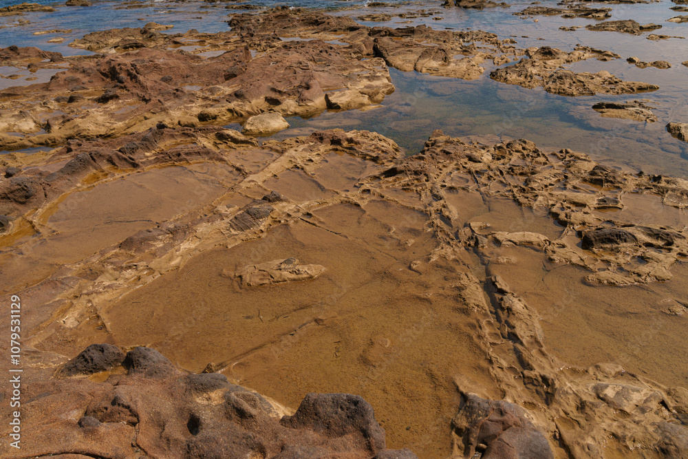 Detailed view of a coastal rock surface displaying natural erosion patterns and shallow tidal pools. The rugged terrain showcases the geological features of the shoreline Detailed view of a coastal rock surface displaying natural erosion patterns and shallow tidal pools. The rugged terrain showcases the geological features of the shoreline