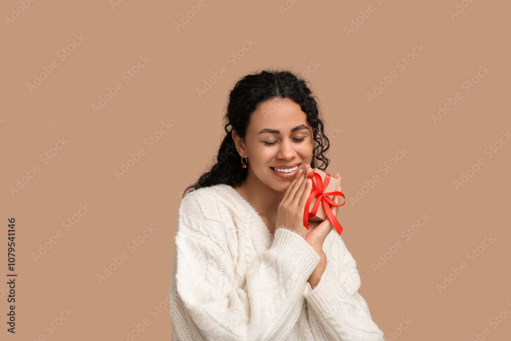 Beautiful young African-American woman in stylish earrings with gift box on brown background. Christmas celebration Beautiful young African-American woman in stylish earrings with gift box on brown background. Christmas celebration