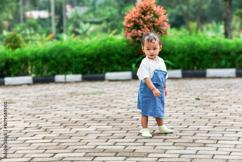 A beautiful Asian little child stands on a stone path surrounded by greenery A beautiful Asian little child stands on a stone path surrounded by greenery