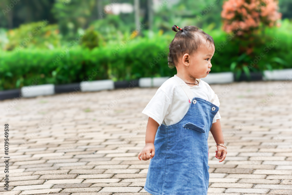 A beautiful Asian little child stands on a stone path surrounded by greenery