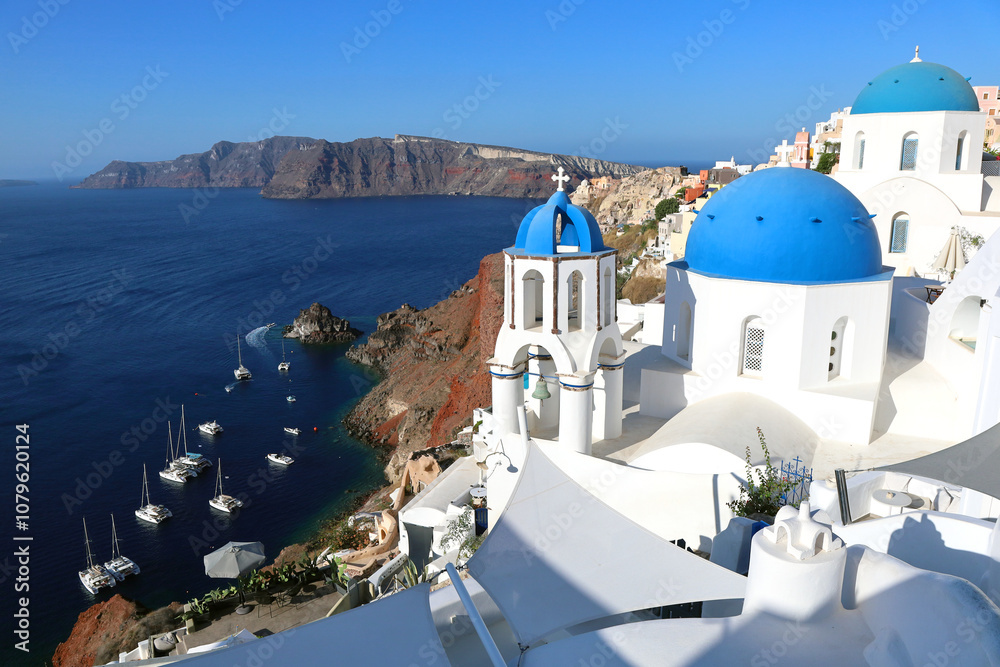 Fototapeta premium Oia Santorini's iconic blue-domed churches overlooking the island's volcanic caldera and the Mediterranean Sea 