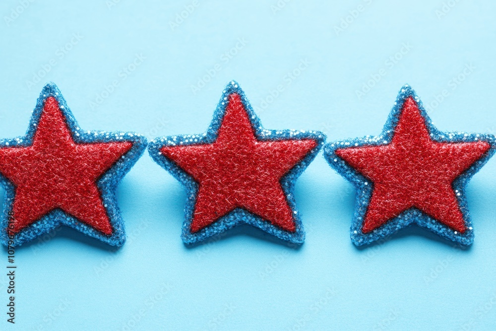 Three red and blue glittery star decorations on a light blue background. Three red and blue glittery star decorations on a light blue background.