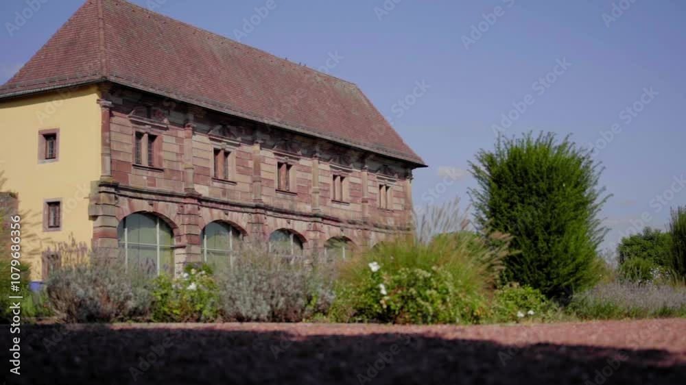 A wide, cinematic slow-motion shot of the historic Blieskastel Orangery surrounded by lush summer greenery and blooming bushes, capturing the essence of traditional European architecture A wide, cinematic slow-motion shot of the historic Blieskastel Orangery surrounded by lush summer greenery and blooming bushes, capturing the essence of traditional European architecture