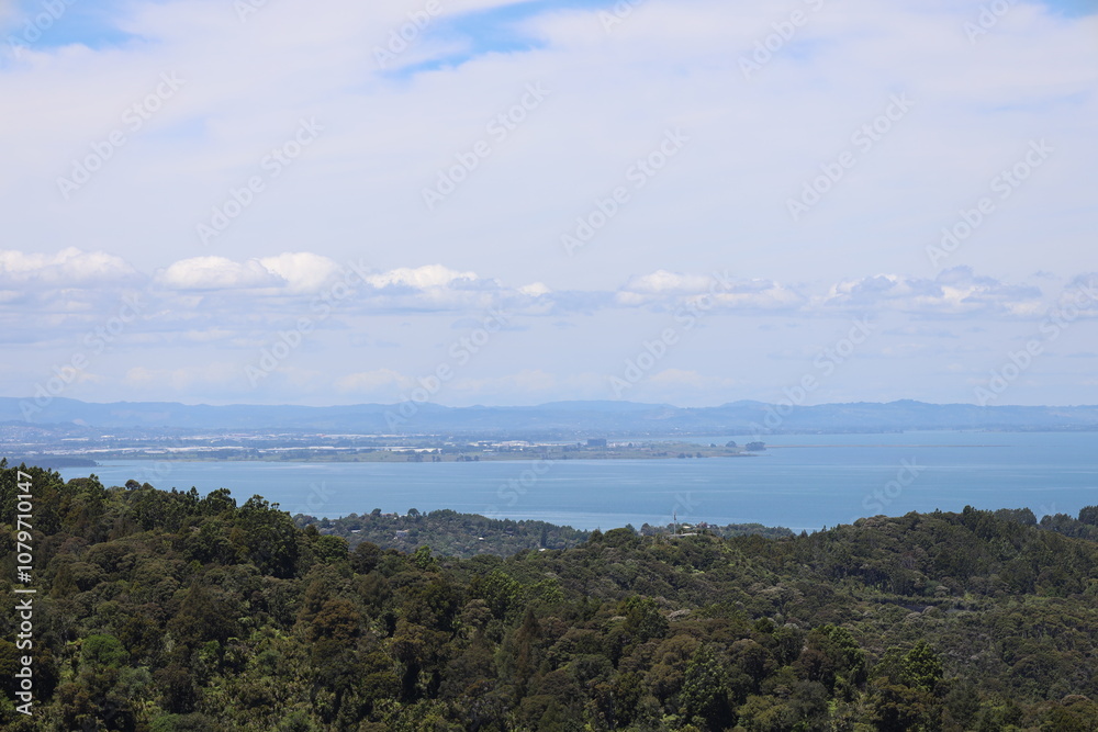 rolling forested hills, blue ocean bay and hills beyond under cloudy sky rolling forested hills, blue ocean bay and hills beyond under cloudy sky