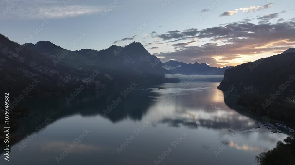 Sunrise over Walensee in Switzerland with mountain reflections on calm water and scattered clouds