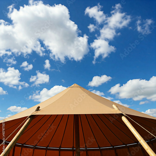 A large, tan tent with a peaked roof under a bright blue sky.