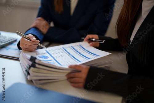 Two businesswomen in a modern office setting, deeply focused on reviewing a document together. Their expressions reflect concentration and a serious approach to the task.