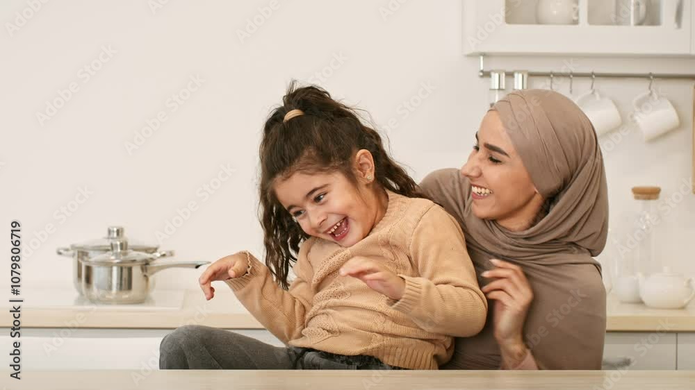 In a bright, modern kitchen, a mother warmly hugs her daughter, both sharing laughter and joy. The interaction highlights their loving bond during a relaxed moment together. In a bright, modern kitchen, a mother warmly hugs her daughter, both sharing laughter and joy. The interaction highlights their loving bond during a relaxed moment together.