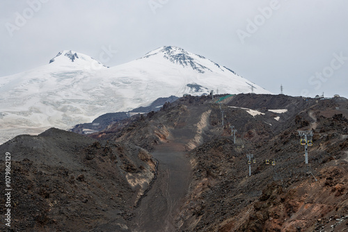 Mount Elbrus, Caucasus Mountains. Kabardino-Balkaria, Russia. Mountain landscape. Two snow-capped peaks of Elbrus are visible in the distance. Gondola lift on a rocky mountainside. Summer, August. photo