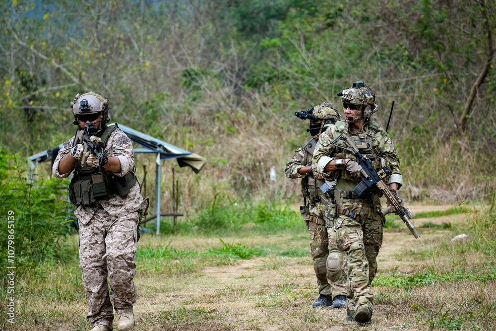 Fototapeta premium A group of military men in combat gear patrol in the middle of a desert and tropical jungle. Soldiers in full combat gear in dry weather conditions assemble and march on a mission.