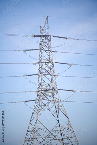 electricity transmission tower under clear sky, high voltage power lines structure, industrial steel pylon for power distribution, tall electricity pole against blue sky, power grid infrastructure in  photo