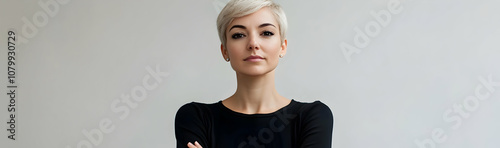 Confident woman with short blonde hair standing with arms crossed against a light background -