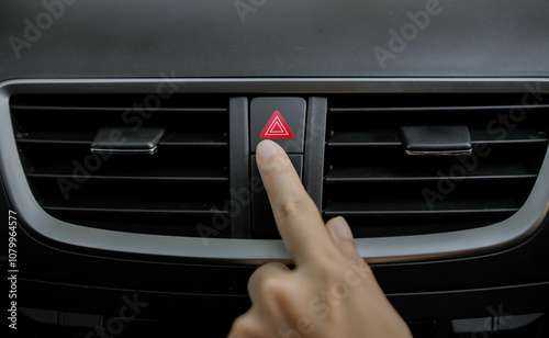 Close-up of female driver's hand pressing the emergency button in car. Emergency light button on the car dashboard