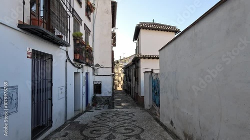 Morning light casts a golden glow over the Albaicin narrow, winding alleys. White Moorish facades bask in tranquil serenity, reflecting the historic charm of this Granada neighborhood. Granada, Spain