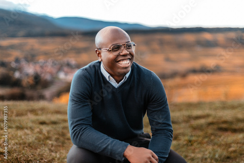 Portrait of a man sitting outdoors, smiling with a scenic landscape in the background. Captures confidence and relaxation in nature