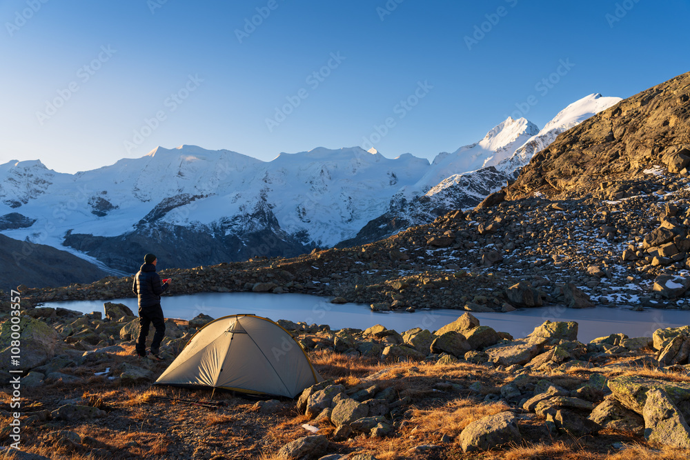 A hiker enjoying his coffee at a beautiful campsite in the Bernina mountain range. Switzerland.