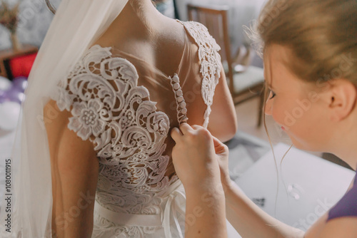 A woman is getting her wedding dress altered by another woman. The bride is wearing a white lace dress and the other woman is adjusting the dress