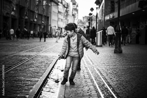 Black and white photo of a child playing near tram tracks in a lively urban street. Captures innocence and exploration in an everyday city setting.
