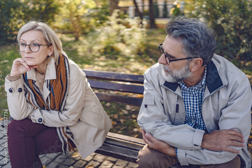 Obraz na plátně Senior couple sitting apart on a park bench in an autumn setting, looking upset