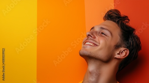 A young man smiles against a vibrant orange and yellow striped wall while enjoying a moment of happiness in a well-lit space