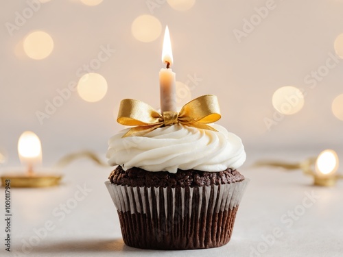 Chocolate cupcake with vanilla frosting and a gold bow, topped with a lit candle