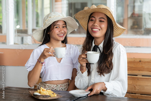 Two young women in stylish hats share a joyful moment with coffee at a cozy cafe, radiating warmth and friendship.