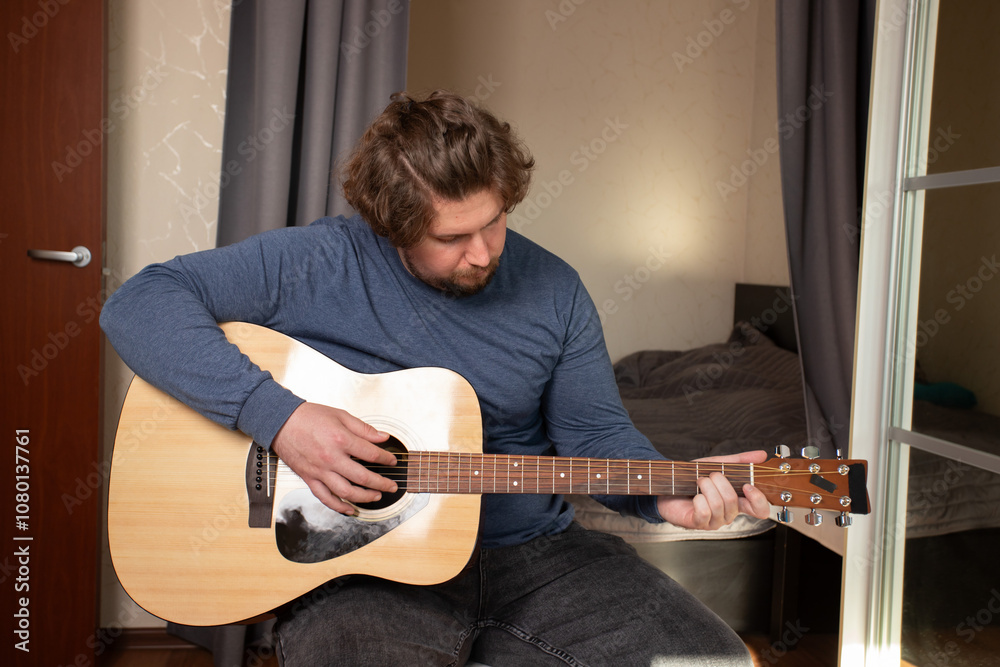 Obraz premium Man Practicing Guitar in Cozy Bedroom, dedicated performer enhancing musical skill, focus on teaching himself through study.