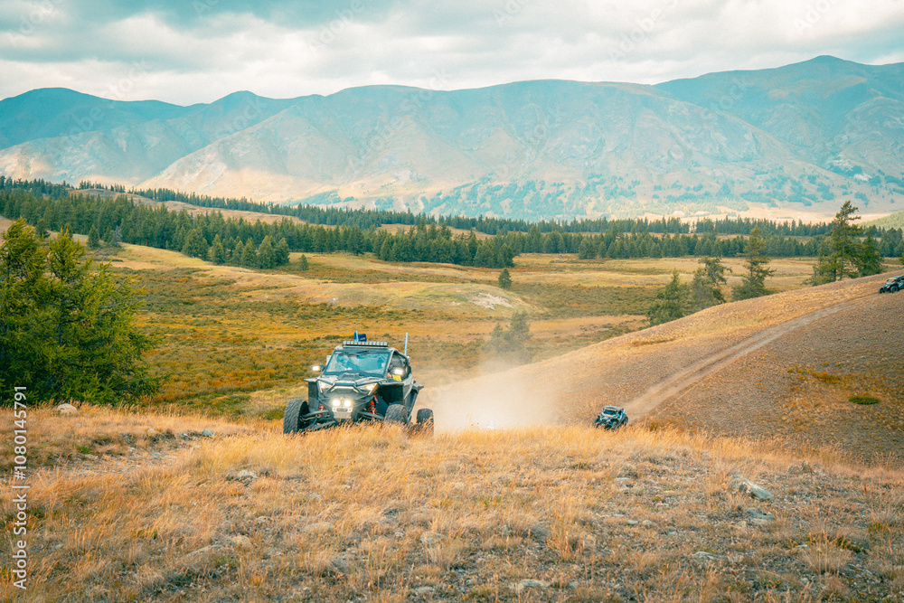 Buggy trip in a Altai desert. Mountain landscape with hills and beautiful blue sky with clouds in background. Off-road vehicles driving on a dust dirt road. Active leisure in Altai Republic. Buggy trip in a Altai desert. Mountain landscape with hills and beautiful blue sky with clouds in background. Off-road vehicles driving on a dust dirt road. Active leisure in Altai Republic.