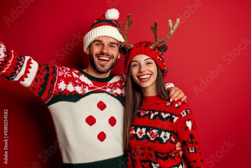 Cheerful holiday selfie  man in snowman sweater and woman in reindeer antlers against red backdrop photo