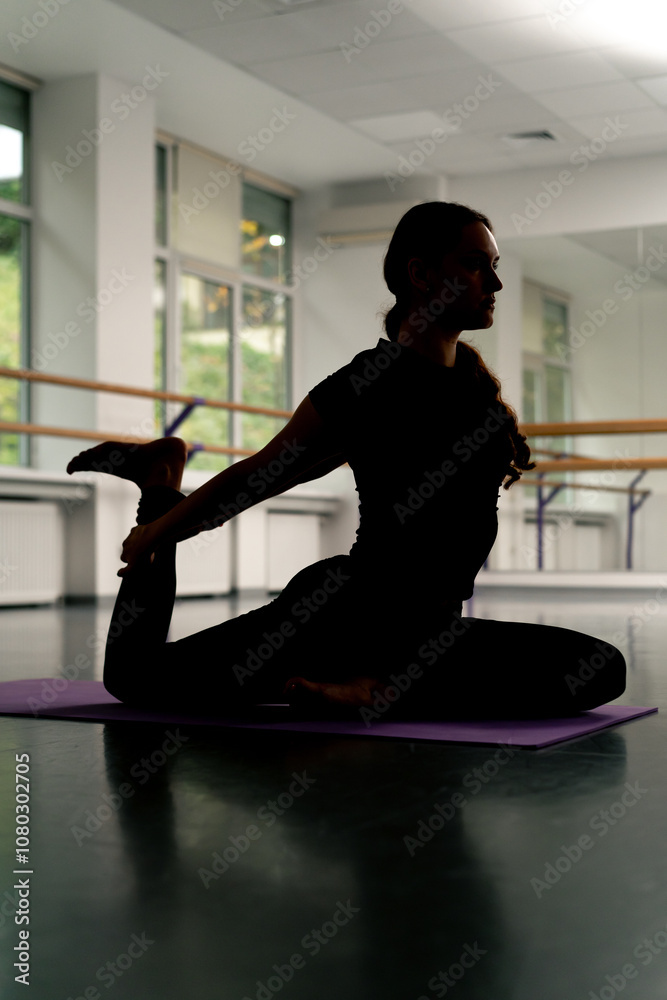 in studio of spiritual development master class on yoga girl with long hair on a purple mat sits pulls leg back pose asana backlight dark silhouette in studio of spiritual development master class on yoga girl with long hair on a purple mat sits pulls leg back pose asana backlight dark silhouette