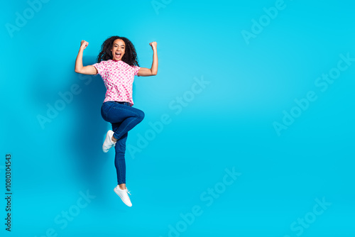 Full length photo of lucky positive girl wear print t-shirt jumping high rising fists empty space isolated blue color background