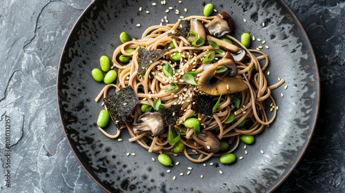 A top-down view of Asian-inspired black truffle pasta with soba noodles, soy ginger sauce, edamame, shiitake mushrooms, nori strips, and sesame seeds.