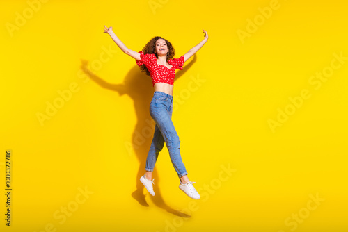 Full size photo of pretty young girl playful jumping have fun wear trendy red outfit isolated on yellow color background