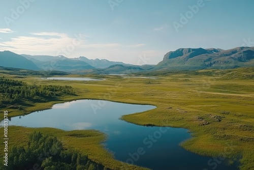 Aerial view of a green field and a lake in Norway, with mountains in the background