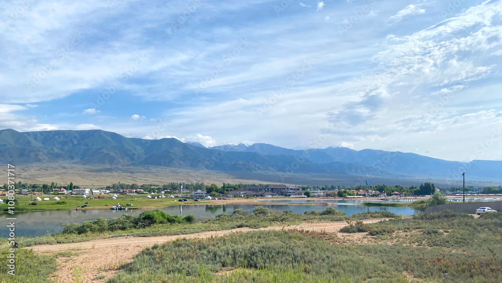 Obraz premium View of a small backwater of the Issyk-Kul mountain lake in Kyrgyzstan, Asia. Rural landscape. Beautiful summer panorama of a small village in the mountains of Kyrgyzstan. Travel and tourism