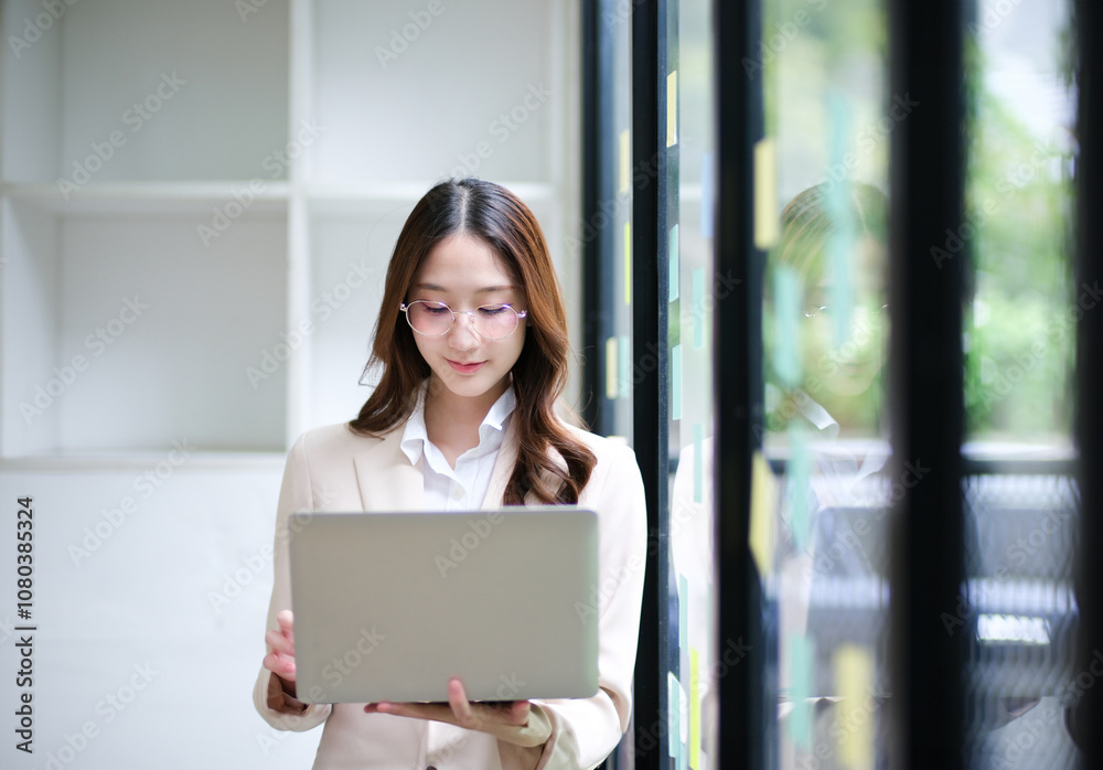 Businesswoman using a laptop and reviewing data with sticky notes in the background. Businesswoman using a laptop and reviewing data with sticky notes in the background.