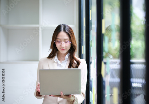 Businesswoman using a laptop and reviewing data with sticky notes in the background.