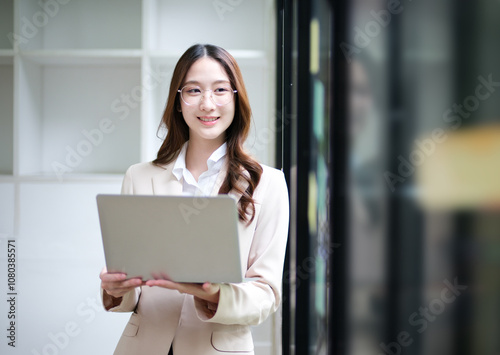 Businesswoman using a laptop and reviewing data with sticky notes in the background.