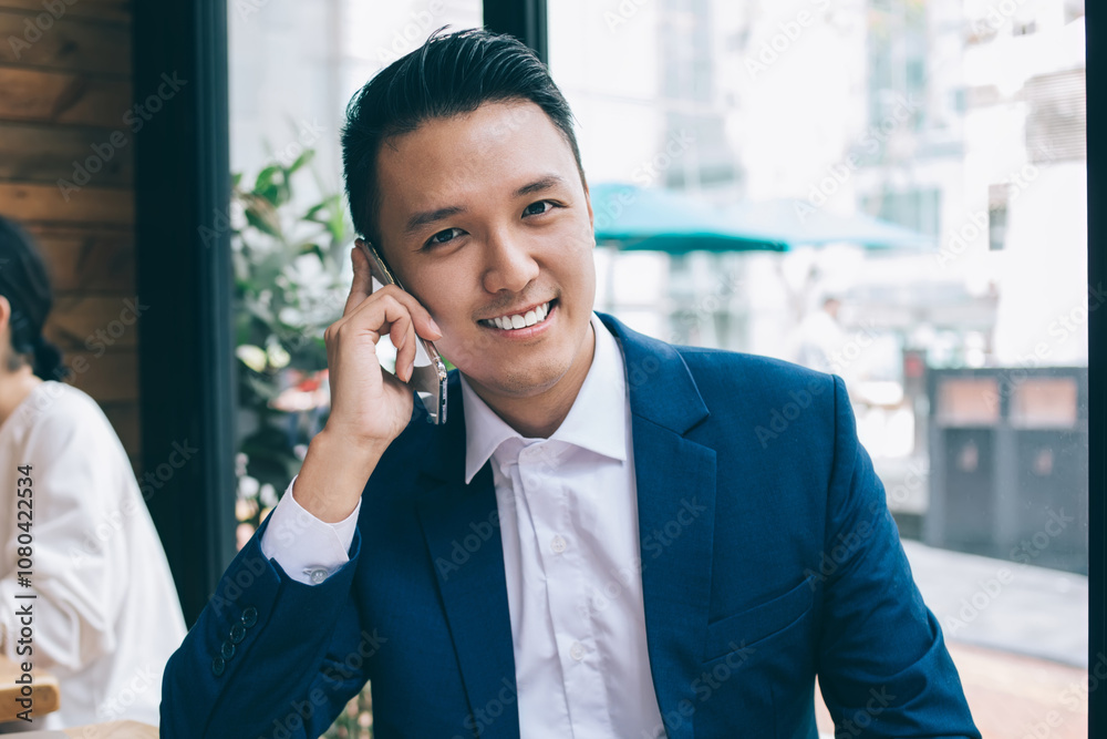 Asian smiling young businessman talking on phone and looking at camera Asian smiling young businessman talking on phone and looking at camera