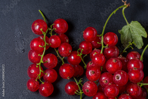 Fresh red currants on a dark, textured surface with water droplets enhancing their vibrant color.